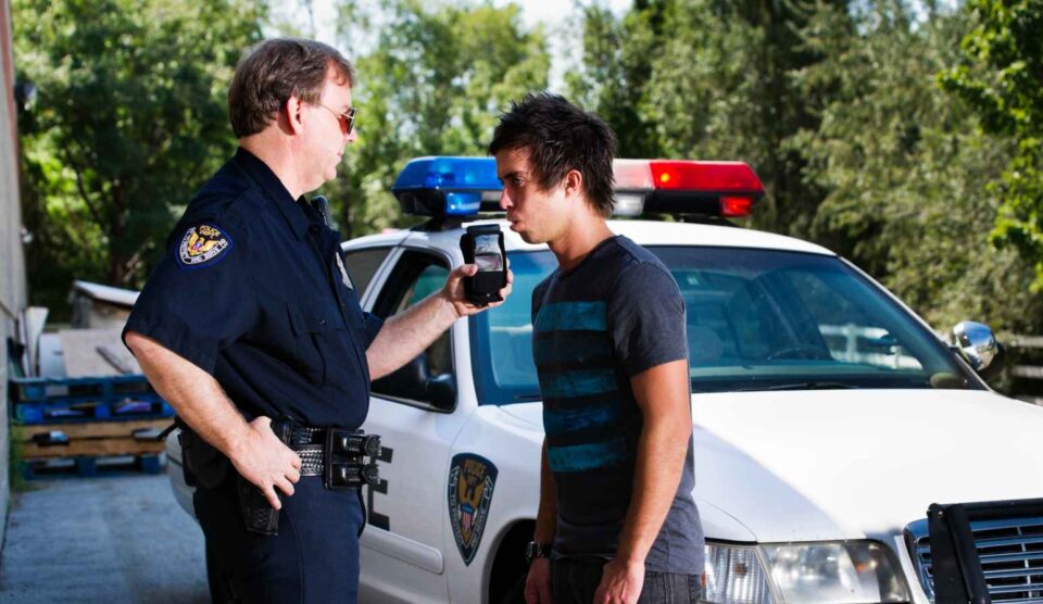 Police officer conducting a breathalyzer test on a young man outdoors