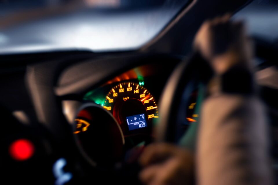 Driver's hand on steering wheel, dashboard showing 90 km/h speed and fuel range